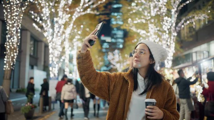 一名兴奋开朗的女子用她的手机拍下了圣诞主题城市的美丽灯光。