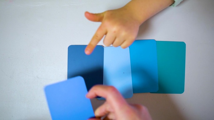 大人的手给孩子看桌子上蓝色的彩色卡片。