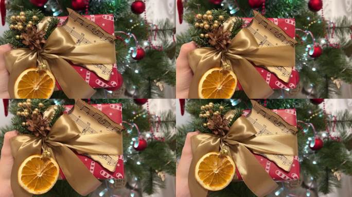 可爱的圣诞礼物包装，上面有一张燃烧过的纸条金棕色的蝴蝶结，干橙色的铃铛，松果，冷杉树枝，红色的包装纸