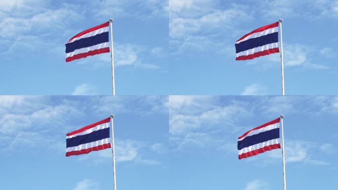 泰国国旗悬挂在白色的高钢杆上，被风吹起，在湛蓝的天空和白云的背景下形成了生动的波浪。