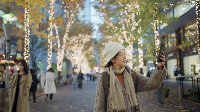 一名亚洲女游客喜欢在圣诞假期散步，并在城市的美丽灯光下拍照。