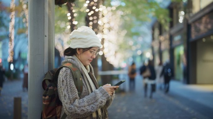 穿着温暖外套的快乐亚洲妇女在冬季集市上用智能手机与家人聊天。