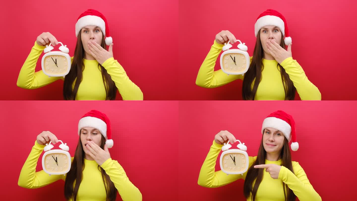 年轻女子穿着黄色毛衣，戴着圣诞老人的帽子，手里拿着食指指着时钟，在红色背景上独自摆姿势。2024年庆