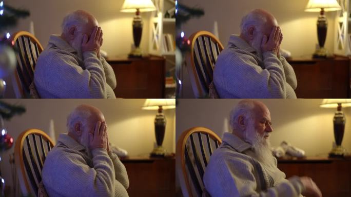 一位留着胡子的老人坐在圣诞树旁的摇椅上，用手捂住脸。