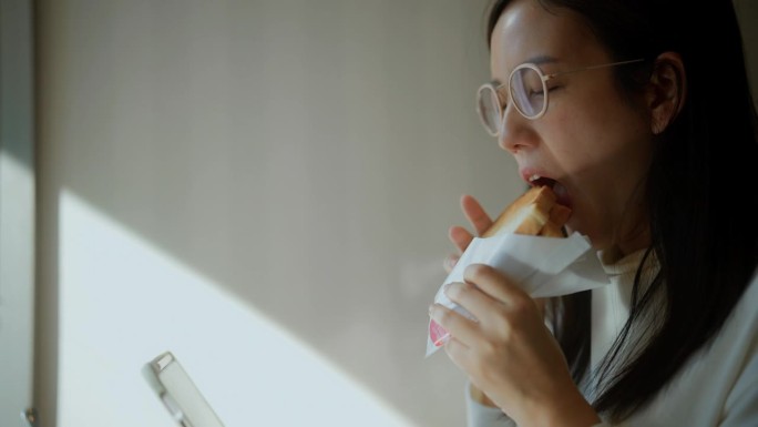 一位女商人一边享用美味的三明治，一边在一家现代化的咖啡店里使用平板电脑工作
