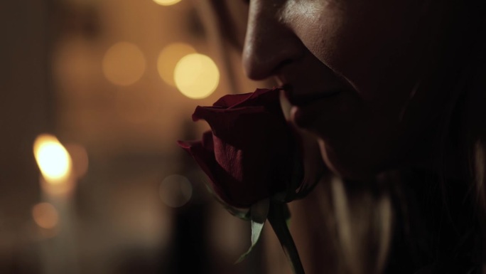 日期，情人节，周年纪念。女人的脸在浪漫的烛光下闻着红玫瑰花的特写