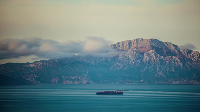 船和云在蓝色的海面上掠过，背景是群山。延时拍摄。