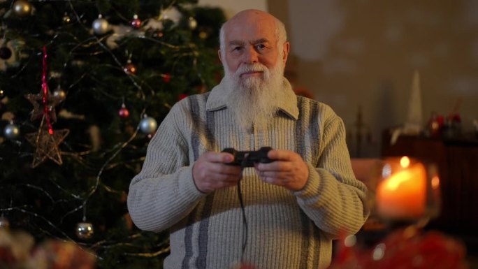 一位大胡子老人站在圣诞树旁，用双手积极地控制着操纵杆，看着屏幕。