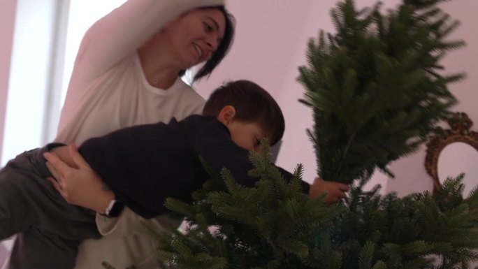 母亲和孩子设置圣诞树-节日季节。妈妈抱起小男孩，把树的一部分放上去
