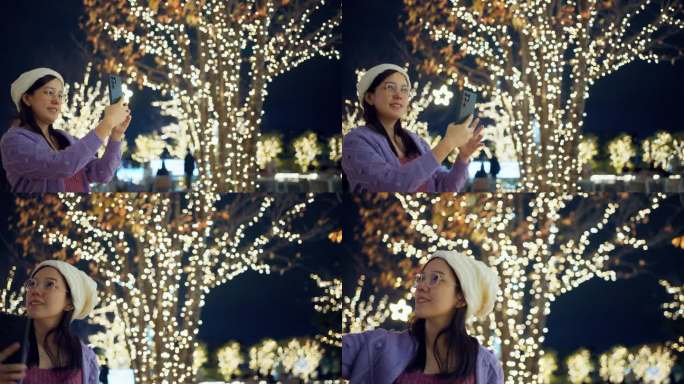 微笑的亚洲孕妇在冬天拿着手机靠近街道的圣诞灯