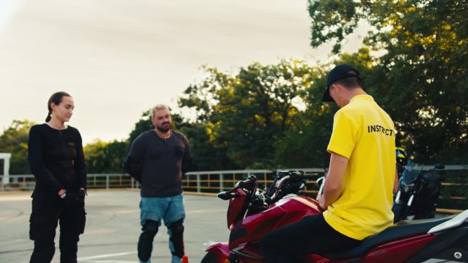 穿着黄色t恤的驾驶教练告诉一男一女如何骑摩托车。学习理论后进行驾驶实践
