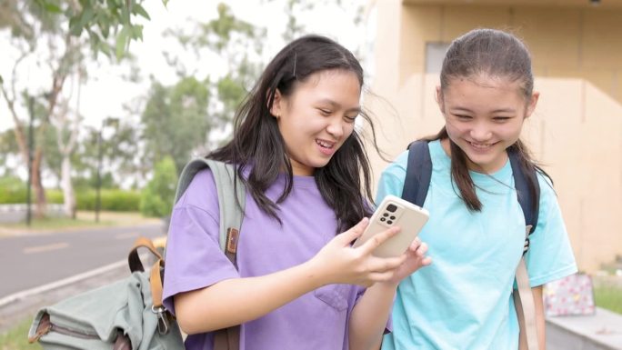 快乐的亚洲学生女孩在学校走路和使用智能手机