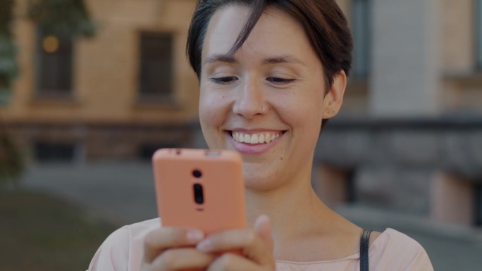 快乐的年轻女子在城市户外查看社交媒体，触摸智能手机屏幕笑