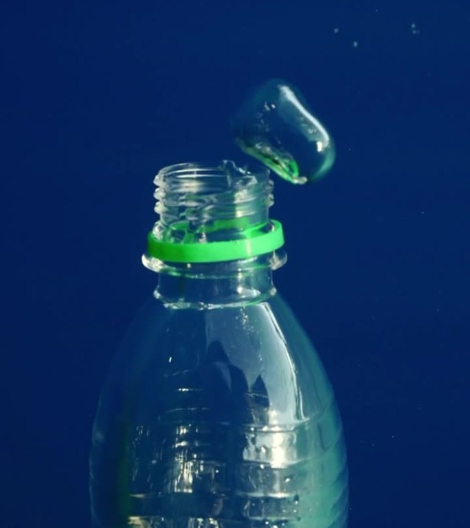 气泡从塑料瓶中冒出来的特写，塑料瓶沉入蓝色深处