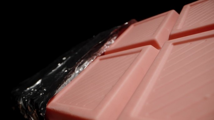 一块大的粉红色巧克力棒，部分从锡箔纸中打开，似乎正在坠入黑暗中。宏变焦。