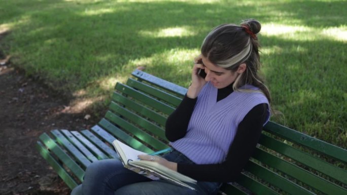 年轻女子在公园边做笔记边讲手机
