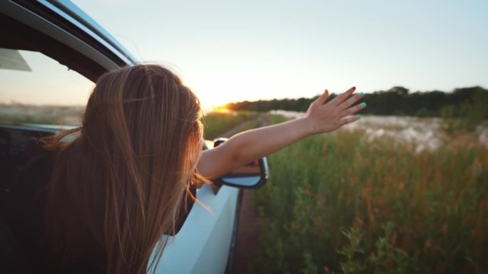 快乐的家庭旅行。小女孩探出车窗挥手。快乐的小女孩把她的手臂伸出开着的车窗外。夏日自驾游概念。