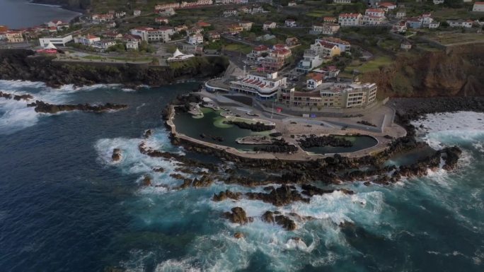 葡萄牙马德拉岛莫尼兹港的火山池，拍摄了悬崖、海洋、自然浴场和日落时的房屋。