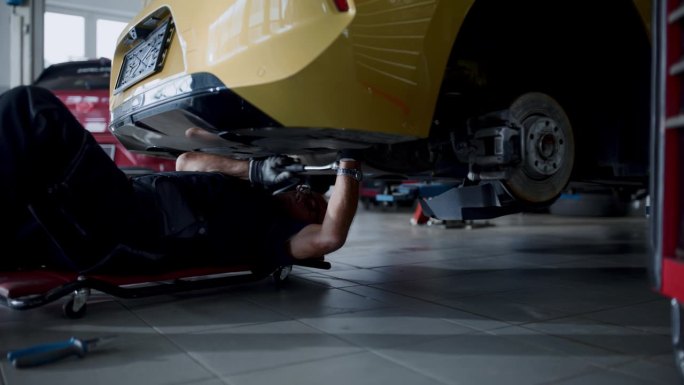 男机械师在汽车修理厂修理汽车下的爬行器