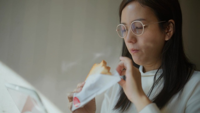 放松的亚洲女人坐在靠窗的咖啡馆享受美味的饭菜