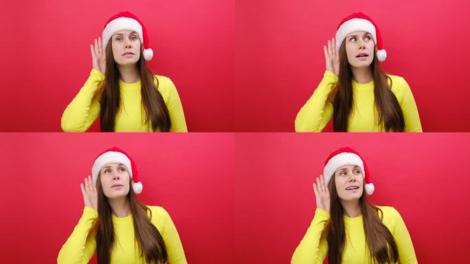 好奇的爱管闲事的年轻女子穿着黄色的毛衣，戴着圣诞老人的帽子，试着听你偷听，在工作室里淡红色的背景下独