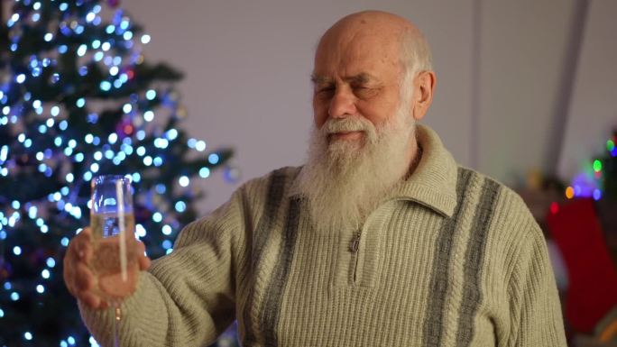 一位白发苍苍的老人端着一杯白葡萄酒在圣诞树旁敬酒。