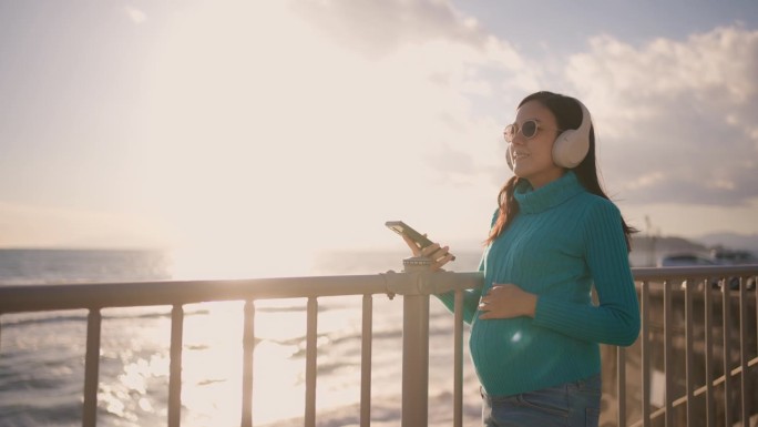孕妇戴着耳机在美丽的河景旁放松音乐