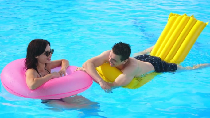一对夫妇，一男一女，在泳池里放松，一起玩耍，享受炎热的夏日。