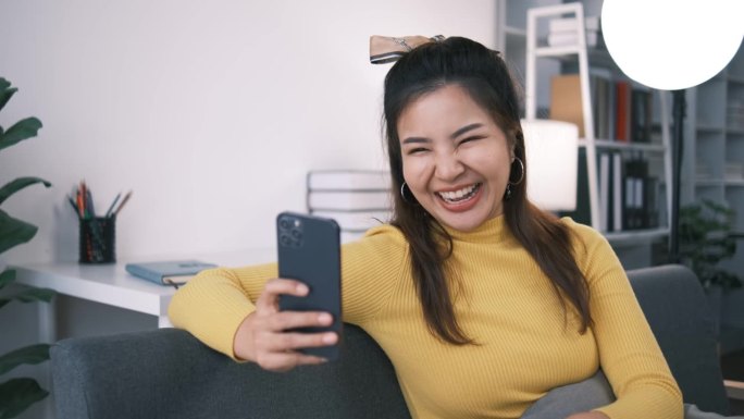 快乐的亚洲少女挥手使用智能手机应用程序享受在线虚拟聊天视频电话与朋友在远程移动聊天虚拟会议，记录故事