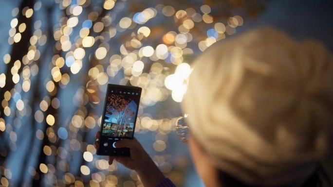 一名亚洲妇女用手机拍摄城市的圣诞灯