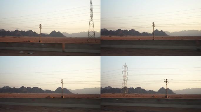 日落时分沙漠中的群山。从快速行驶的汽车的侧面看，前景是架空的电线