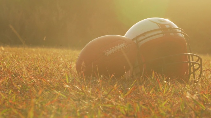 夕阳下戴着防护头盔和球的美式橄榄球运动员。