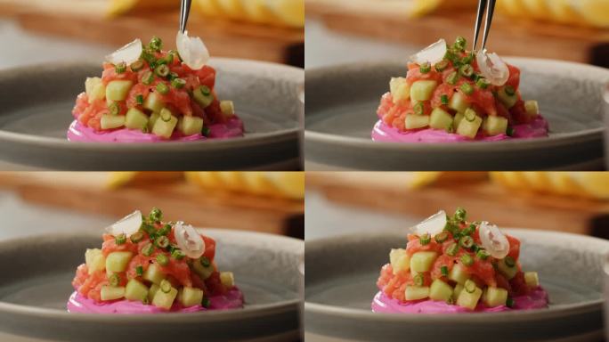 智利三文鱼塔塔服务，牛油果和黄瓜在紫色奶油奶酪上加入绿色和白色的洋葱，洋葱是健康的饮食食品，靠近红色