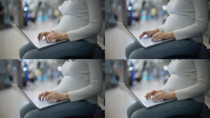 亚洲孕妇坐在机场用笔记本电脑工作。