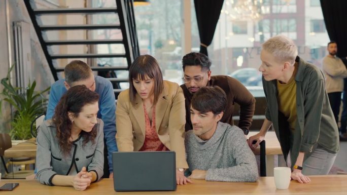 在充满活力的创业公司办公空间里，多元化的团队在笔记本电脑上合作。