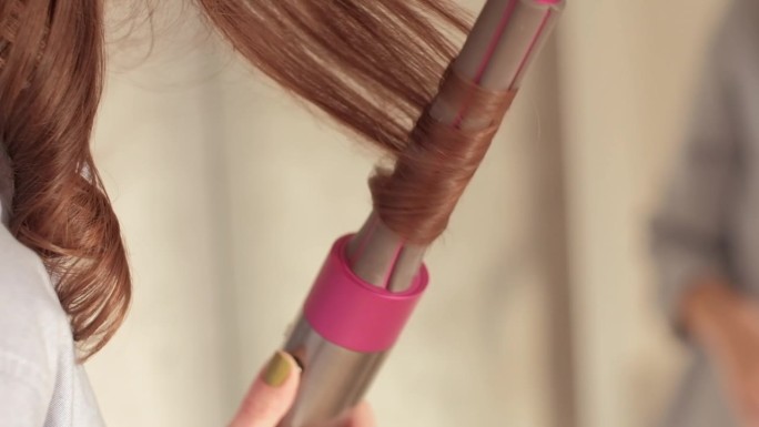 一头卷发的黑发女人，用粉红色的卷发棒把一缕头发卷起来