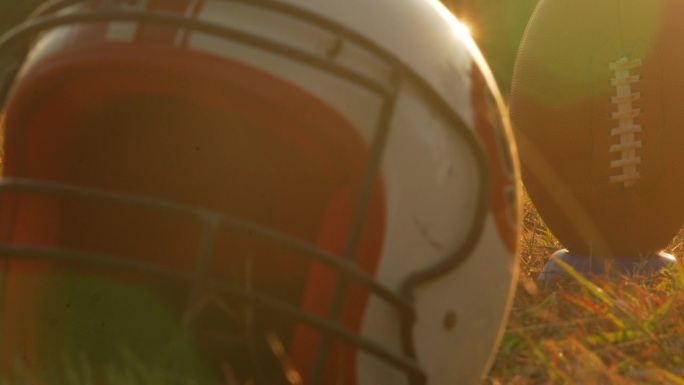 夕阳下戴着防护头盔和球的美式橄榄球运动员。