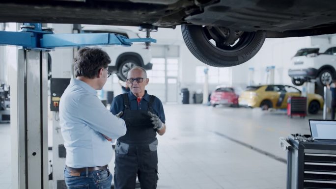 机械师和经理在汽车修理厂的汽车下谈话