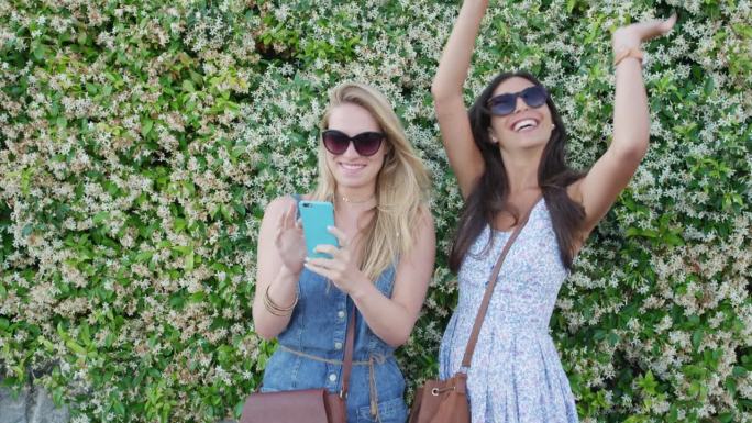 最好的朋友在意大利度假用智能手机发短信女孩们用手机分享生活照片站在鲜花墙前发短信欧洲度假旅行冒险