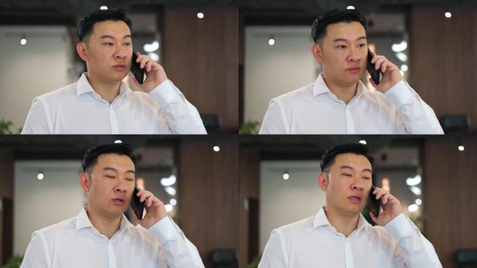 亚洲商人在公司办公室用智能手机交谈的特写，表情严肃。穿白衬衫的成功男士与客户讨论约会的时间和日期。