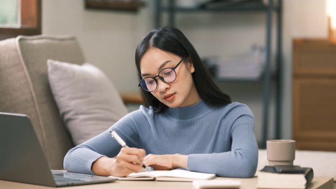 年轻的成年亚洲女学生在家里用笔记本电脑做笔记。亚洲女性在线学习听力虚拟视频通话。商业和教育理念。