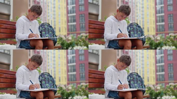 帅哥放学后坐在长凳上不情愿地做作业。悲伤的年轻男生在外面写着课本，准备考试。儿童与教育理念。