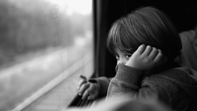小男孩坐在火车座位上，目不转睛地看着窗外的风景。儿童旅行和白日梦的黑白场景