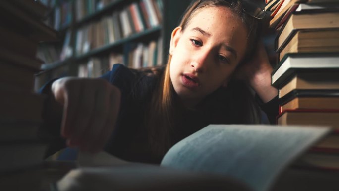 教育的概念。一个女学生在图书馆里靠着书架看书。一个十几岁的女孩正在图书馆里看书。孩子在图书馆做作业。