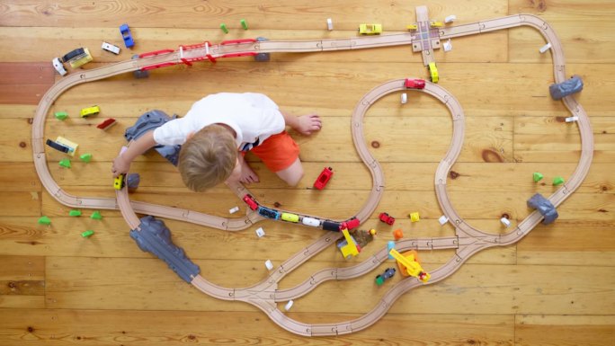 可爱的孩子在家里或幼儿园的地板上玩木制铁路玩具。俯视图