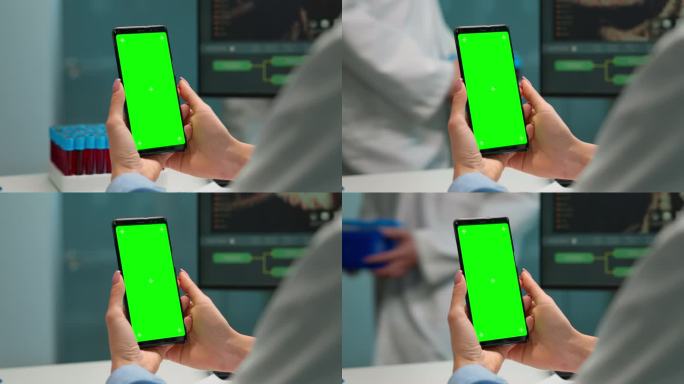 医生坐在办公桌前拿着绿屏手机的特写