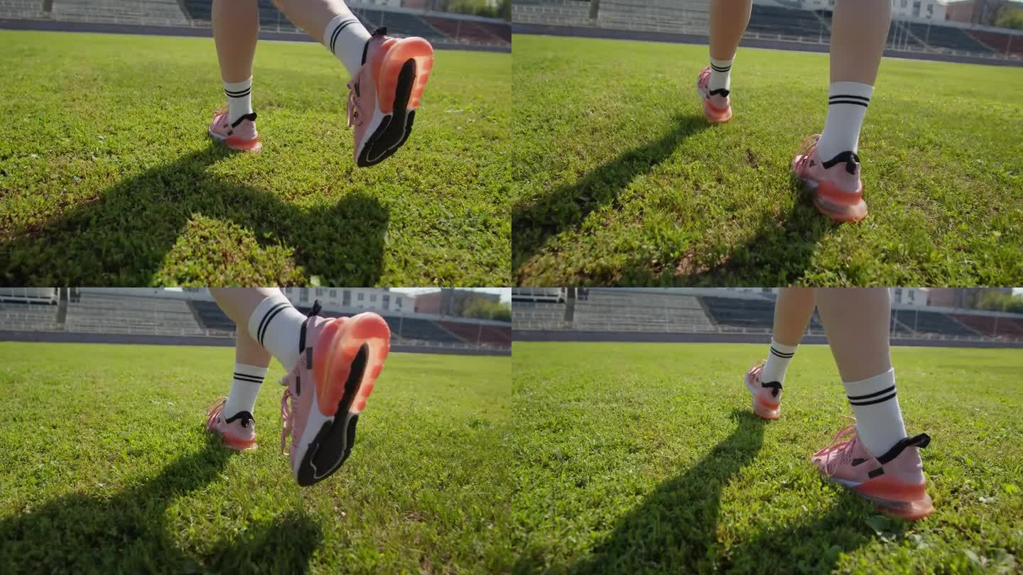 女子穿着白袜子和粉色运动鞋走在绿色的草地上。年轻女子把她的运动包和垫子放在体育馆的草坪上。腿部特写