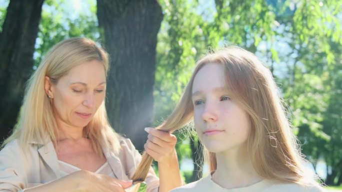 在春天的公园里，尽职的母亲熟练地为十几岁的女儿编织头发