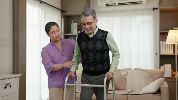 老夫妇在客厅用助步器帮助学习走路。家庭关系概念，夫妻，关怀，健康，疾病