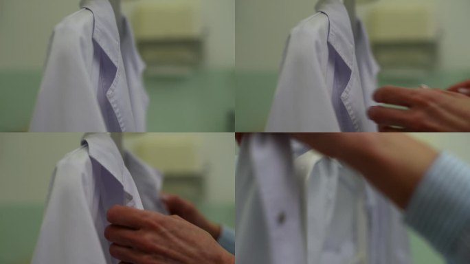 特写镜头，无法辨认的女医生从衣架上脱下白大褂，自己穿上。专业从业者准备工作